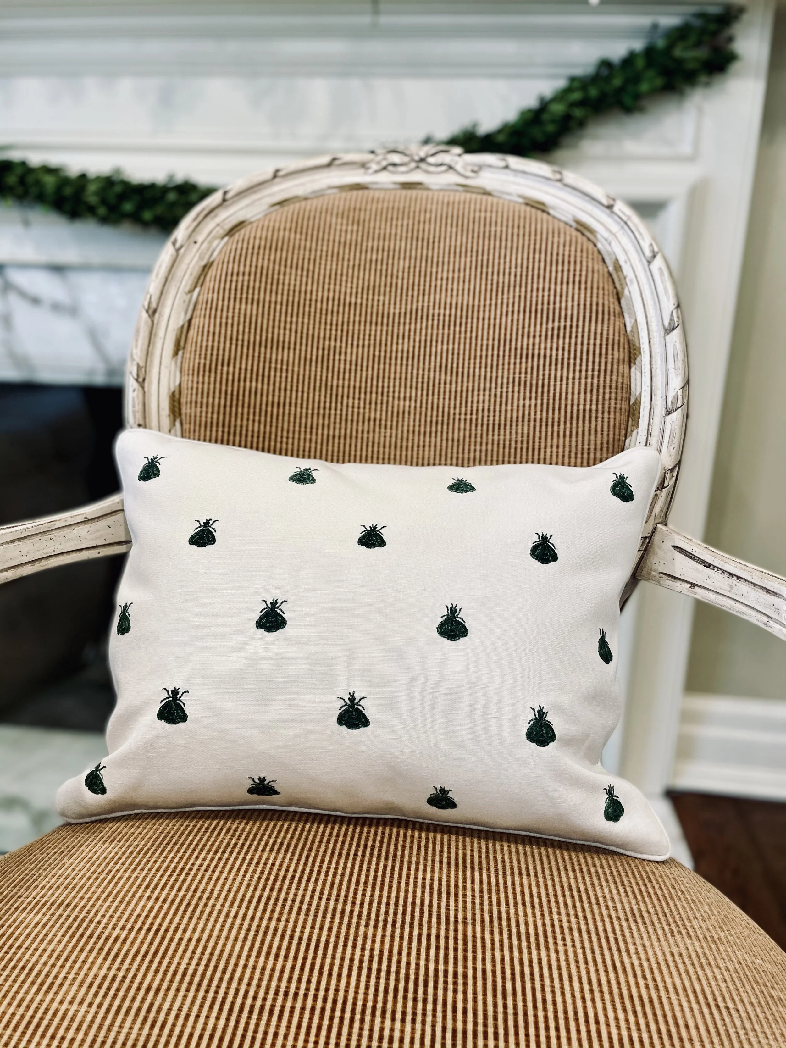 Green-on-cream bee pillow on a French cane chair