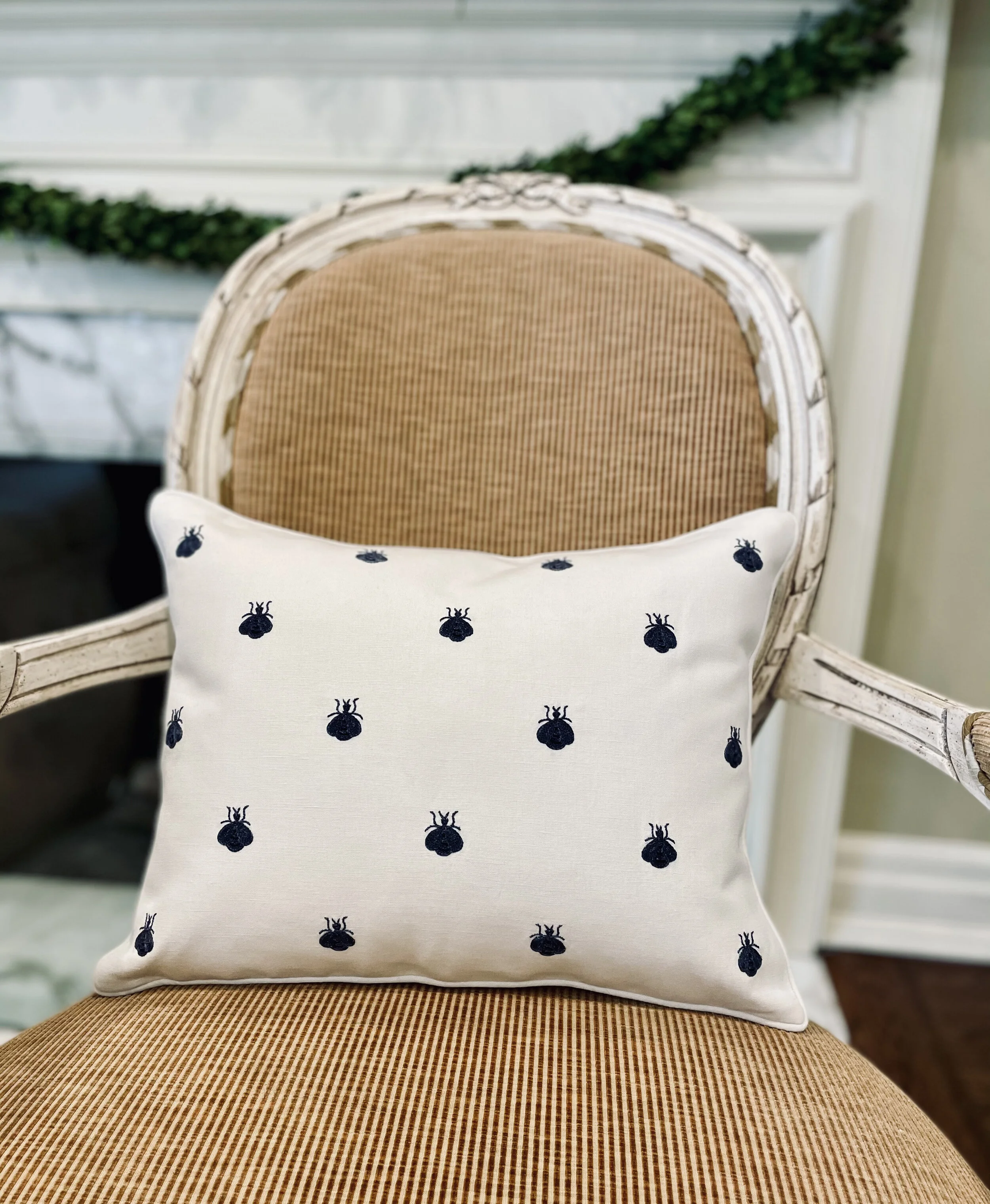 Navy-on-cream bee pillow on a French cane chair